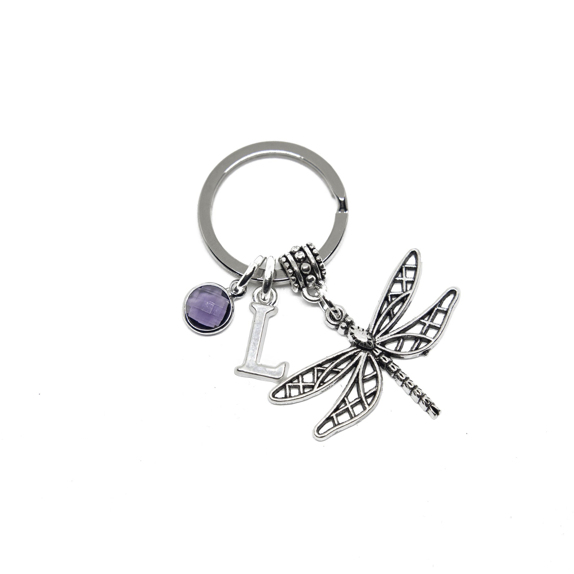 A silver-colored keyring featuring a dragonfly charm, a letter charm, and a small birthstone charm, attached to a split ring.