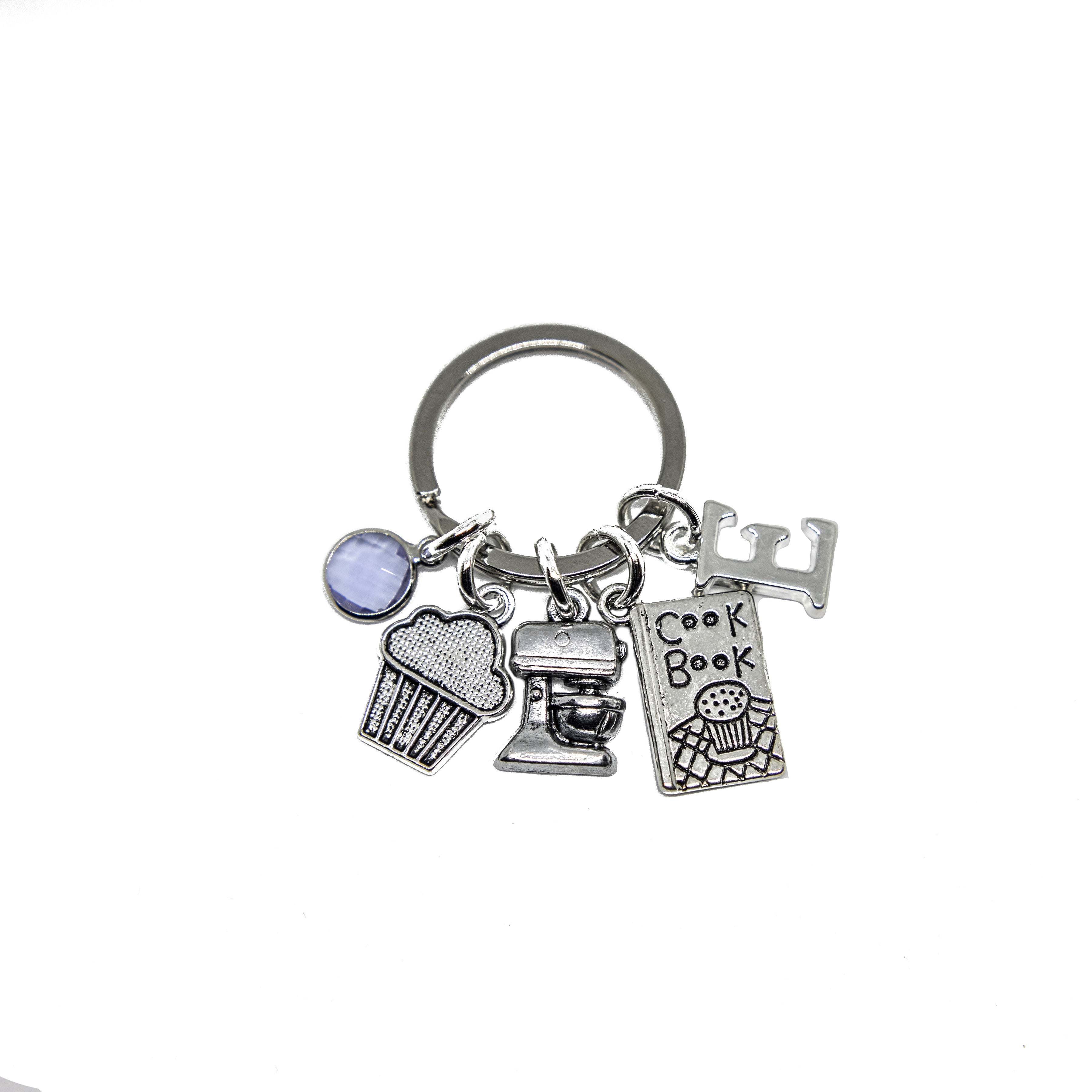 A keyring with silver metal alloy charms including a birthstone, a cupcake, a food mixer, a cook book, and a letter charm.