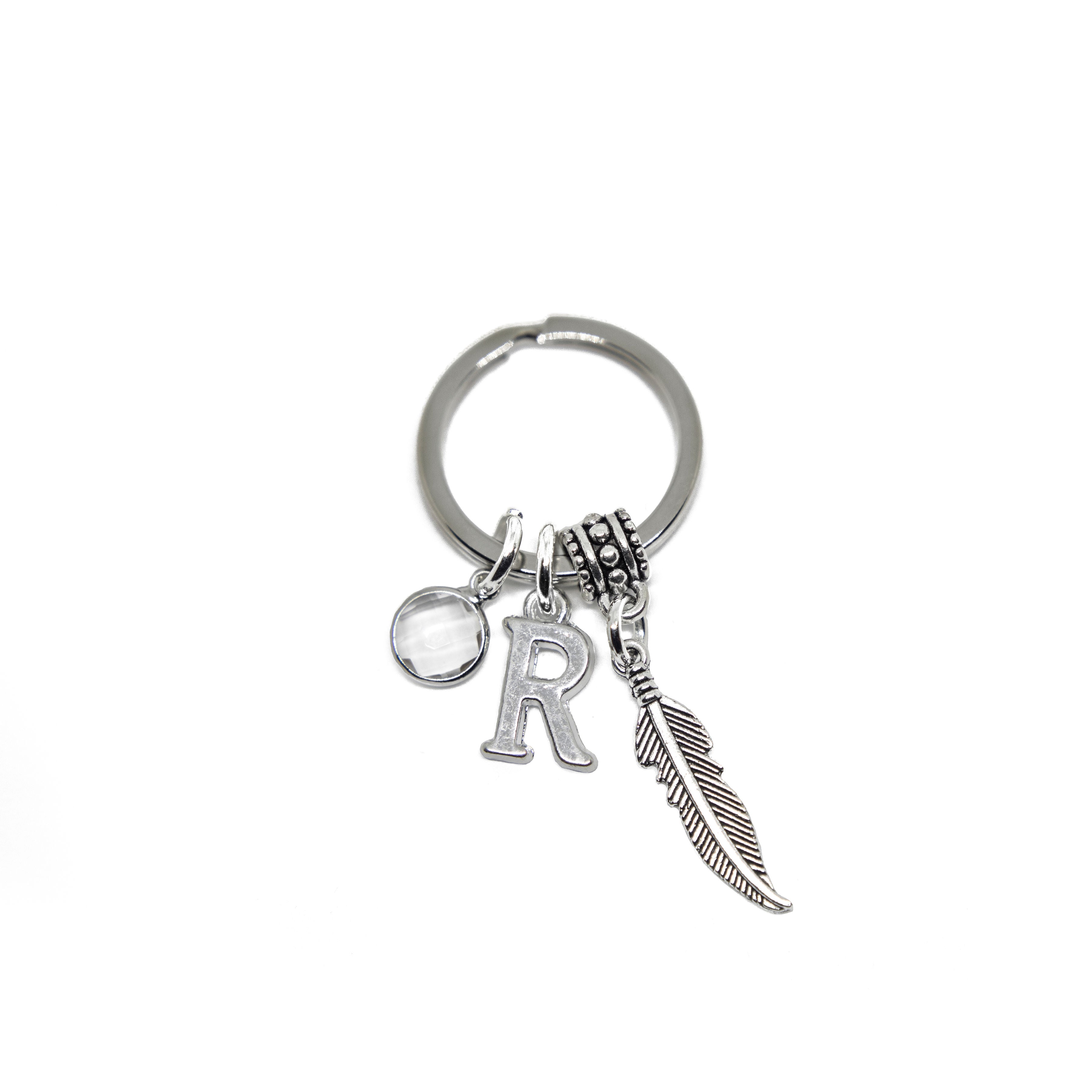 A silver keyring with a feather charm and two additional charms, one with a birthstone and another with a letter, attached to it.