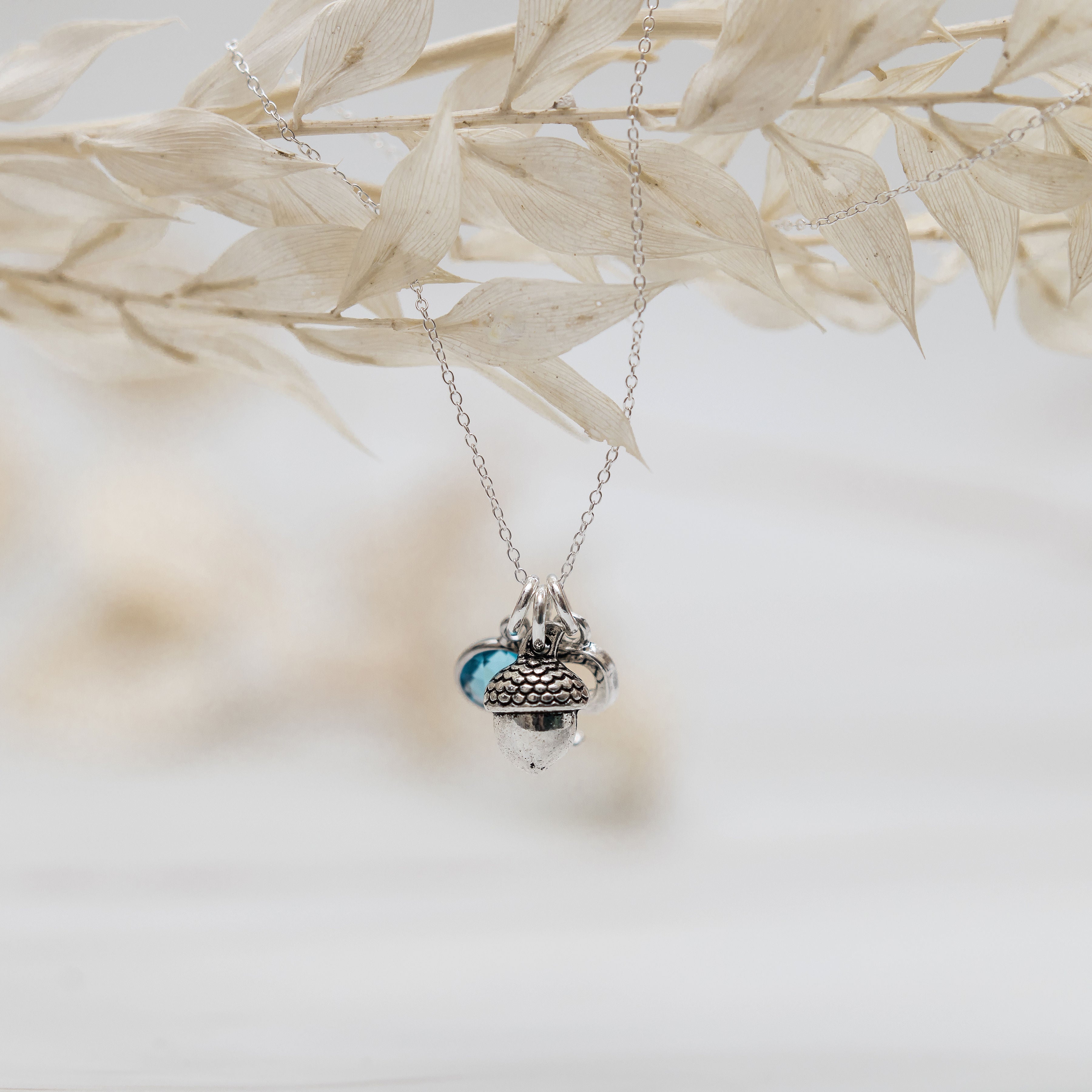 Customised pendant necklace with a trio of charms on a dainty trace chain. The necklace has a birthstone charm, then an acorn charm and then a letter charm.