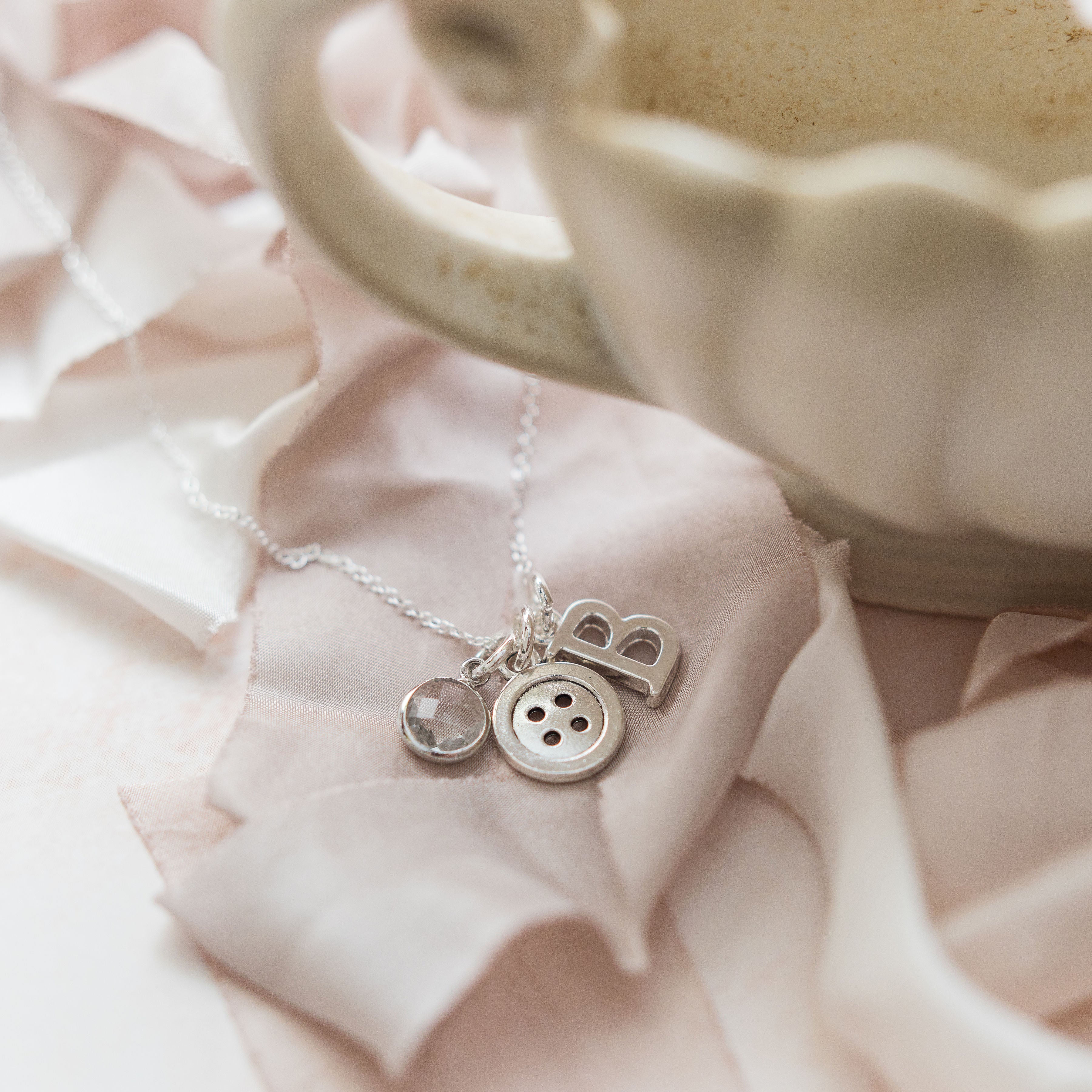 The necklace has three charms, the first charm is a birthstone charm, the second charm is a round button, the final charm is a letter charm.