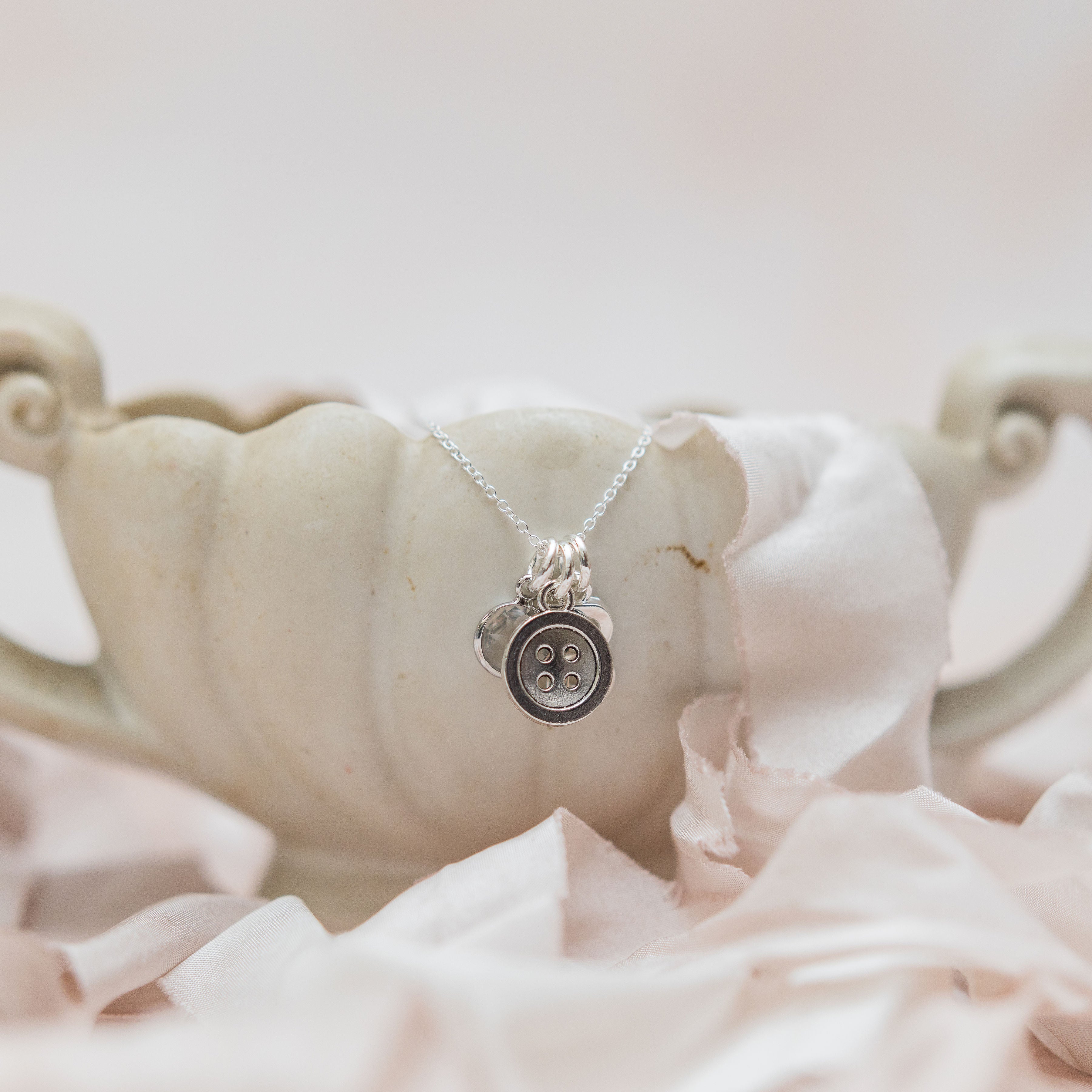 The necklace has three charms, the first charm is a birthstone charm, the second charm is a round button, the final charm is a letter charm.