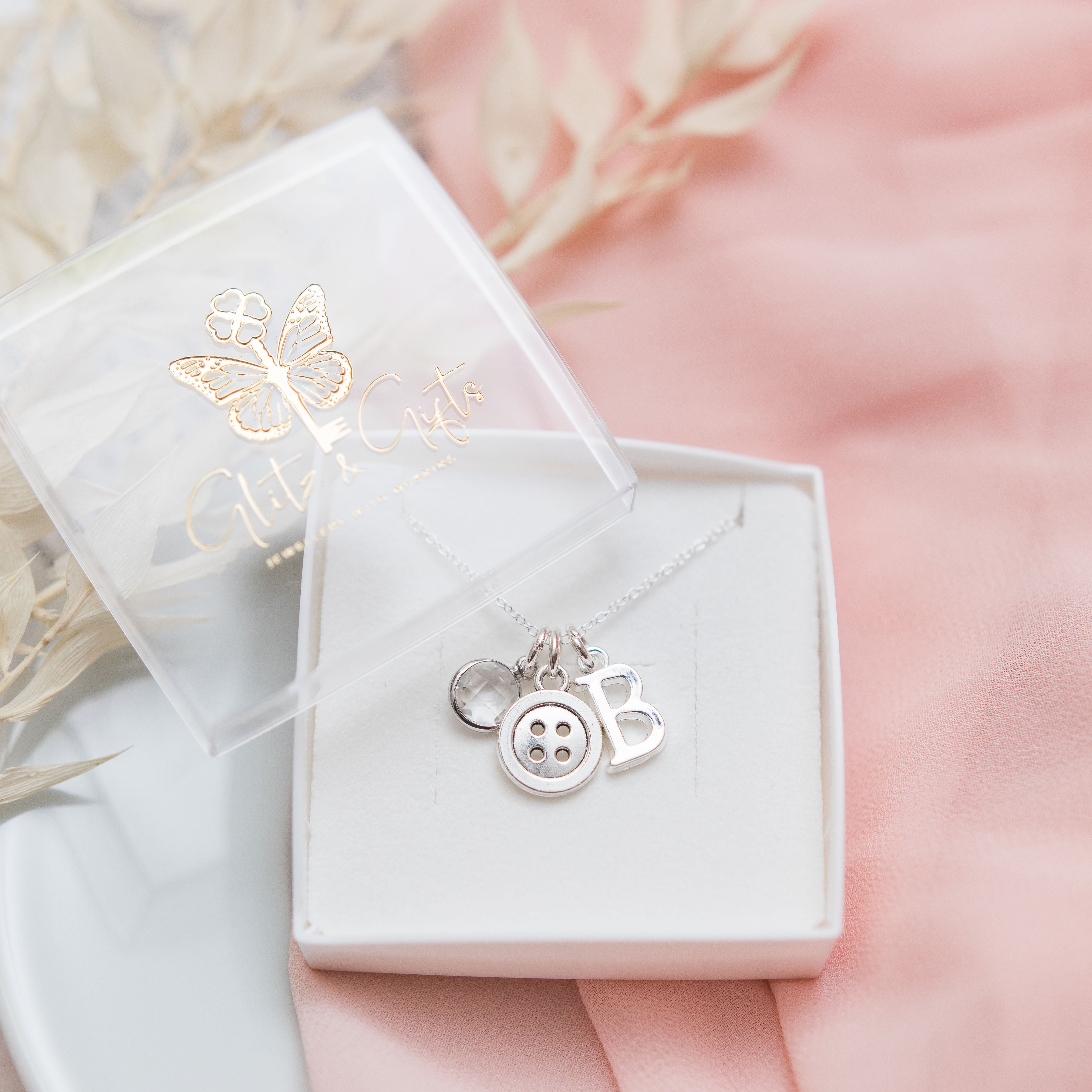 Necklace in gift box. The necklace has three charms, the first charm is a birthstone charm, the second charm is a round button, the final charm is a letter charm.
