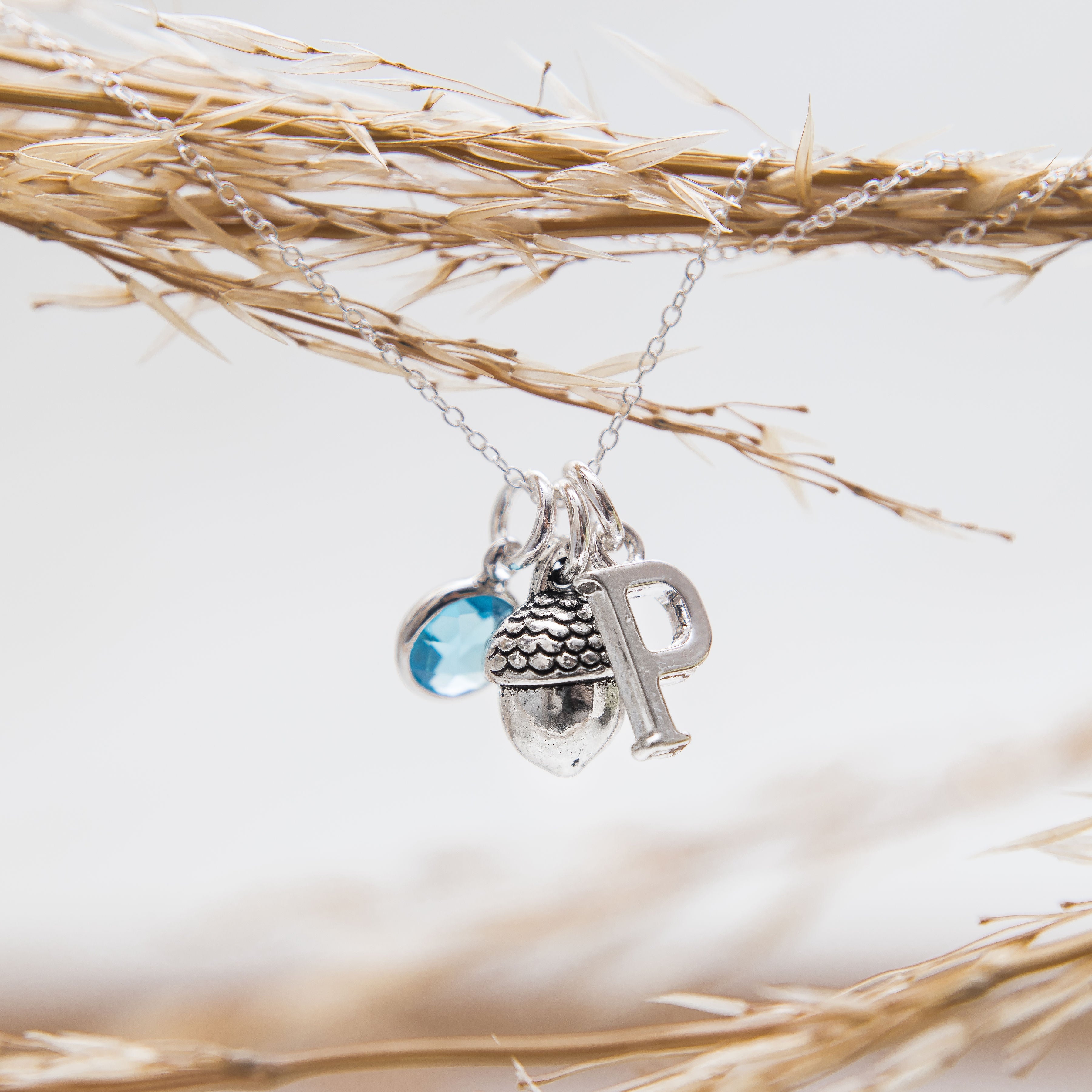 The necklace has a birthstone charm, then an acorn charm and then a letter charm. The charms freely move along the chain, to create a casual style.